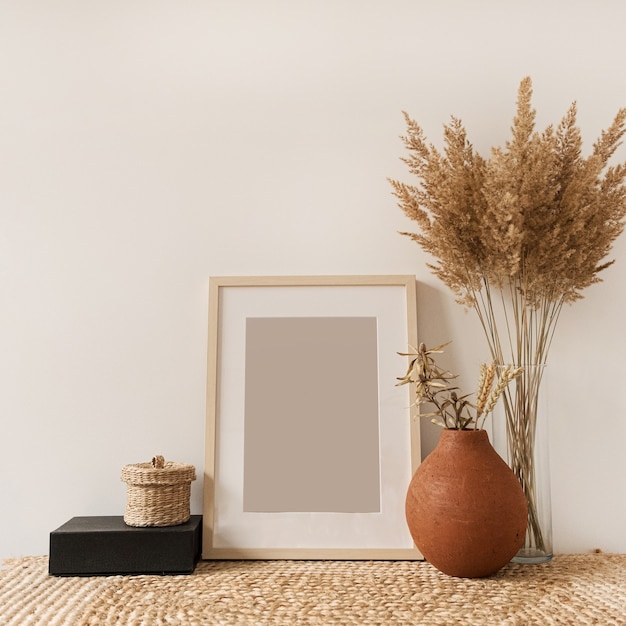 Portafoto vuoto, bouquet di canne soffici in vaso, segale in vaso di terracotta al muro bianco