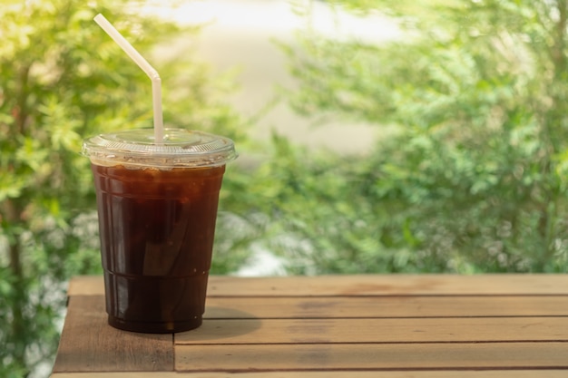 portare via la tazza di plastica di caffè nero ghiacciato (Americano) sul tavolo di legno.