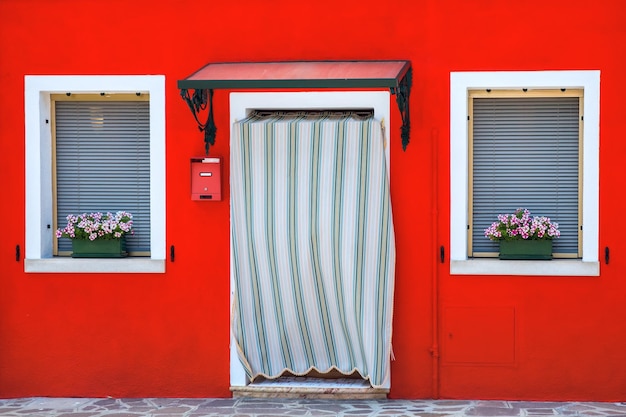 Porte e finestre pittoresche con persiane e fiori sulla parete rossa della casa sulla famosa isola di Burano Venezia Italia