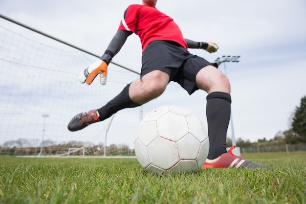 Portiere in rosso calciare palla lontano dalla porta