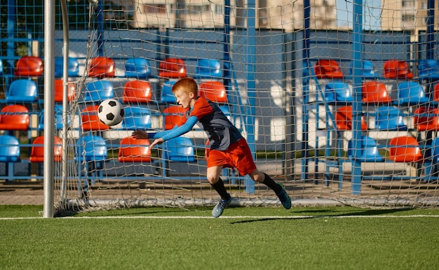 Portiere junior che prende palla mentre difende il cancello nella partita di calcio. Pratica della squadra di calcio o torneo di competizione