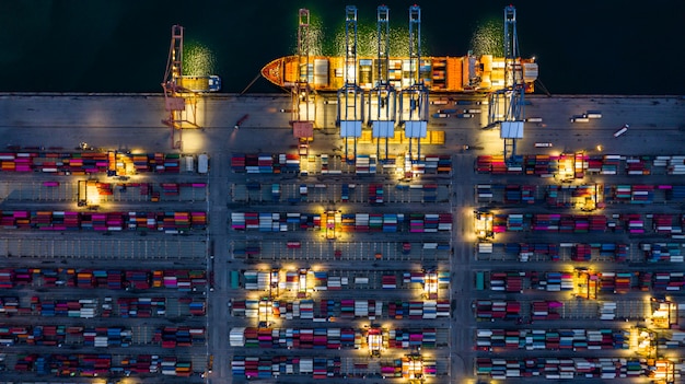 Porto marittimo industriale che lavora alla notte con la nave porta-container che lavora alla notte, nave porta-container di vista aerea che carica e che scarica alla notte.