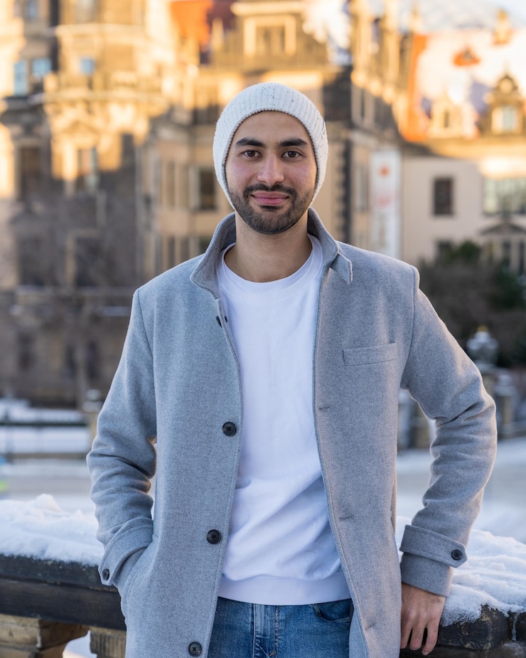 Photo portrait of a handsome young man smiling asian man with a neat beard stands near a wall and looks at the camera