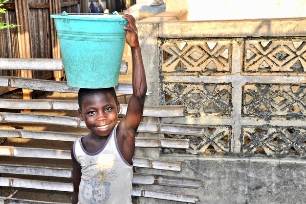 portrait of smiling boy standing with bucket outside home