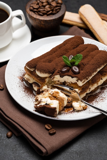 Porzione di dessert tiramisù classico e tazza di caffè espresso fresco su fondo o tavola concreti