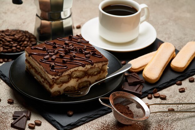 Porzione di dessert tiramisù italiano tradizionale e caffettiera moka sul tavolo di cemento grigio