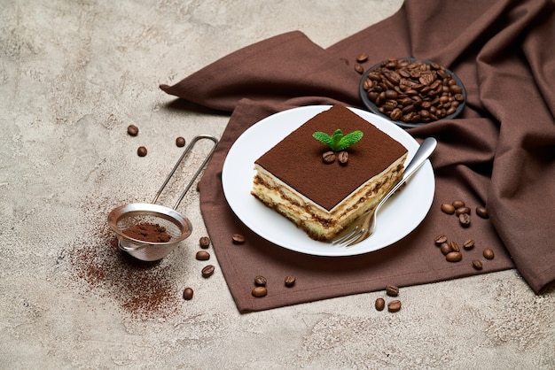 Porzione di dessert tiramisù italiano tradizionale e chicchi di caffè sul tavolo di cemento grigio