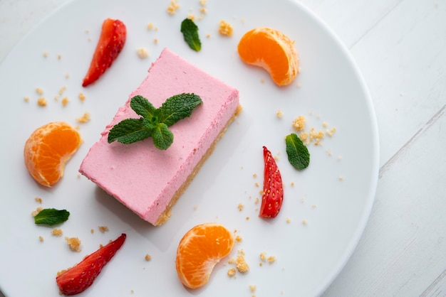 Porzione di mousse alla fragola con base di biscotto servita con frutta fresca e mandarino