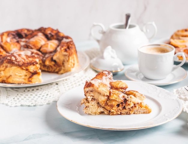 Porzione di panini alla cannella fatti in casa su un piatto bianco su un tavolo bianco con caffè e panini di pasticceria