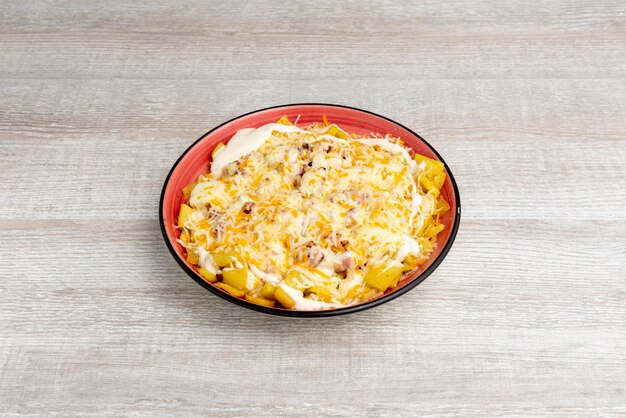 Porzione di patate ranch fritte con crema di formaggio cheddar e formaggio grattugiato con pancetta fritta su un piatto rosso