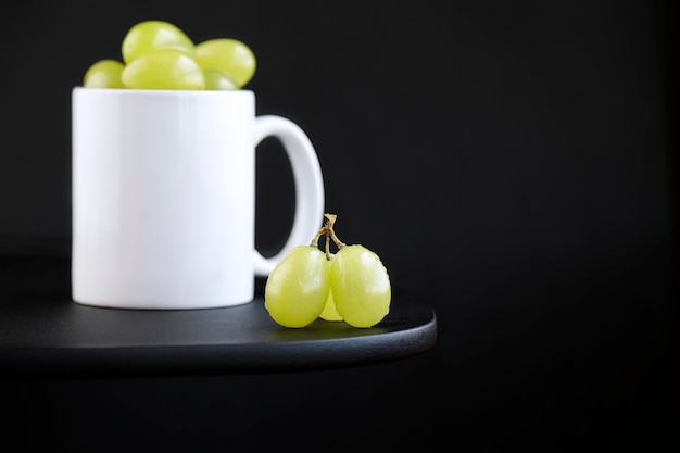 Porzione di uva verde all'interno di una tazza bianca su sfondo nero