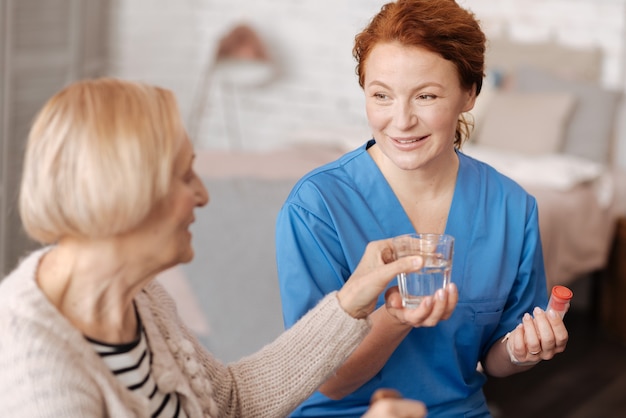 Porzione giornaliera. Specialista privato di spicco qualificato che si prende cura della signora anziana e le dà un bicchiere d'acqua mentre si sottopone a un corso di cure mediche