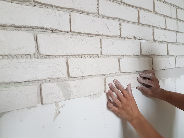 Posa di piastrelle di gesso in file sulla parete con mani maschili.