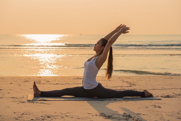 Posa di pratica di yoga della giovane donna in buona salute di yoga sulla spiaggia all&#39;alba