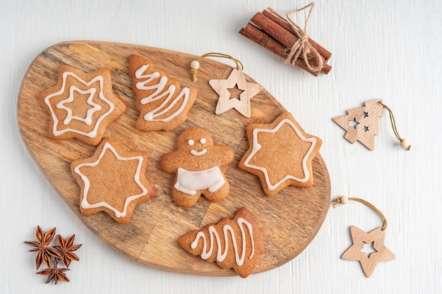 Posa piatta con biscotti di pan di zenzero dolci fatti in casa con glassa di zucchero su tavola di legno su tavolo bianco