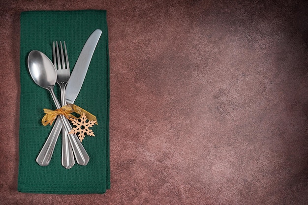 Posa piatta con stoviglie d'argento di forchetta, coltello e cucchiaio servite su tovagliolo verde legato con fiocco