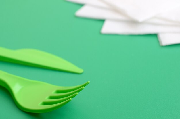 Posate di plastica usa e getta verde. La forchetta e il coltello di plastica si trovano su una superficie di fondo verde accanto ai tovaglioli