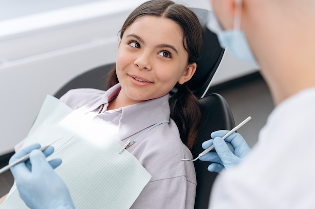 Positiva bambina seduta su una poltrona del dentista. Il dentista controlla i denti di un giovane paziente