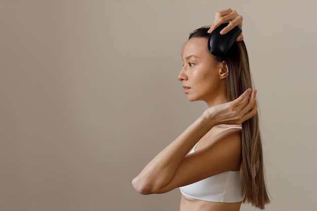 Positiva giovane donna sorridente in top bianco pettina i suoi lunghi capelli lisci sani e ben curati Prodotti cosmetici per la cura dei capelli e del corpo Cura del corpo sana Immagine della ragazza di profilo su sfondo isolato