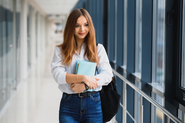 Positività bella ragazza che sorride alla macchina fotografica, in piedi sul corridoio con le note come zaino, andando a lezione