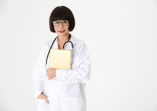 Positivo amichevole giovane donna asiatica specialista medico in camice bianco e occhiali con stetoscopio e tablet sorridente e guardando la telecamera