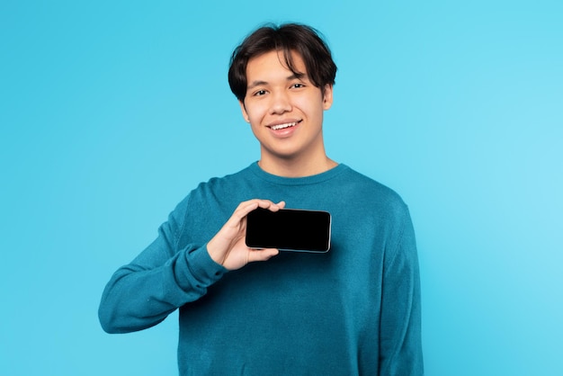 Positivo Asian Teen Guy Holding Smartphone che mostra lo sfondo blu dello schermo