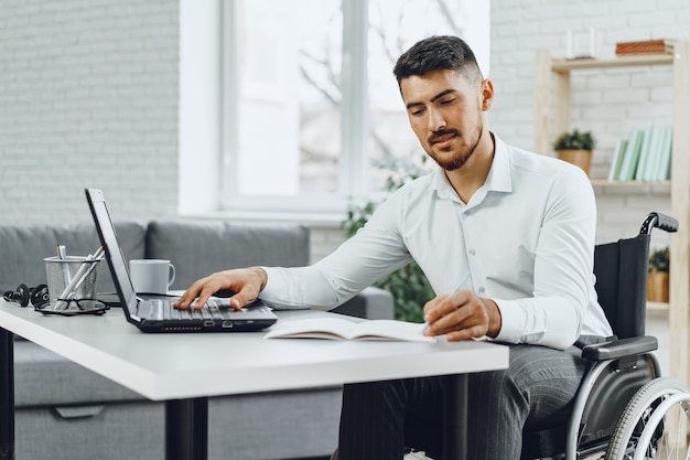 Positivo giovane disabile in sedia a rotelle che lavora in ufficio con il computer portatile