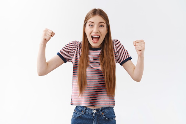 Positivo incoraggiato carino bella donna in maglietta a righe alzando le mani stupito pugno pompa e trionfando guardando intensa partita di calcio sorridente felice sfondo bianco