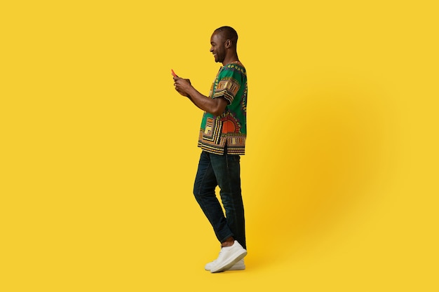 Positivo uomo africano maturo in costume tradizionale tramite telefono cellulare