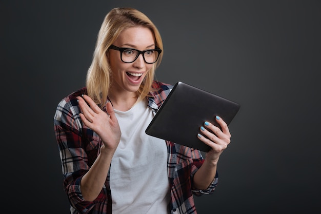 Possibilità infinite. Affascinante simpatica signora amichevole che utilizza un tablet per effettuare una videochiamata mentre lo tiene tra le mani