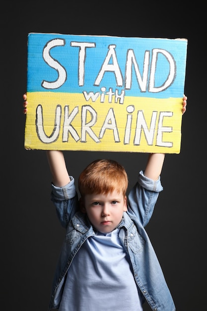 Poster della holding del ragazzo Stand con l'Ucraina su sfondo nero