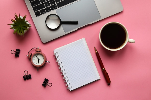 Posto di lavoro alla moda con la lente d'ingrandimento della pianta della sveglia della penna del blocco note del computer portatile e la tazza di caffè