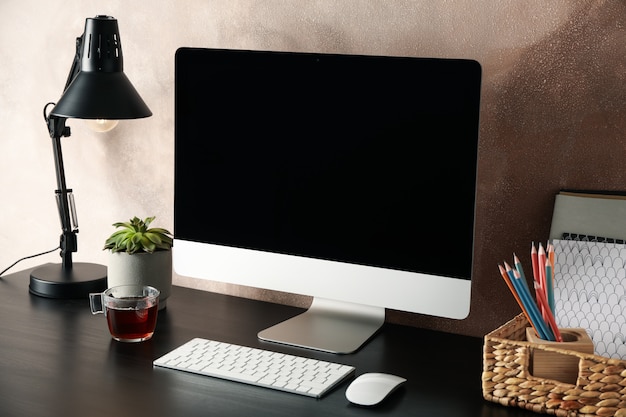 Posto di lavoro con computer, pianta e lampada sul tavolo di legno.