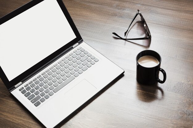 Posto di lavoro con laptop aperto, caffè e accessori sul tavolo dell&#39;ufficio.