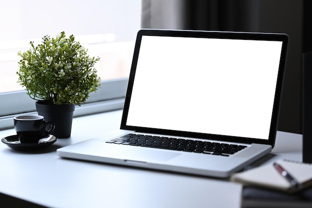 Posto di lavoro confortevole con computer portatile tazza di caffè pianta in vaso e libri sul tavolo bianco