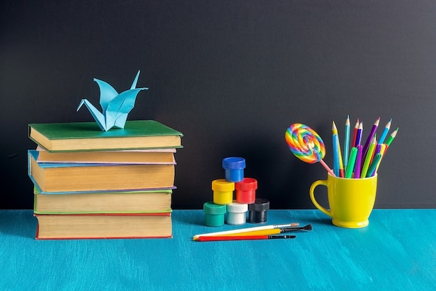 Posto di lavoro degli alunni La gouache e la gru di origami della cancelleria dei libri crane sulla tavola blu