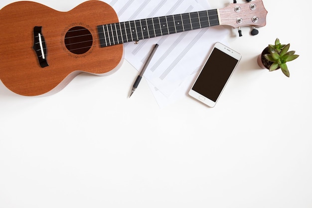 Posto di lavoro di un musicista con un ukulele su uno sfondo bianco, vista dall'alto, copia dello spazio.