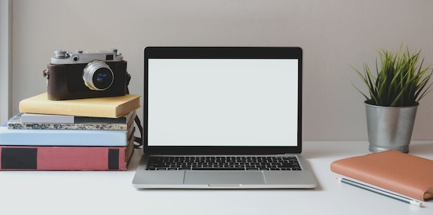 Posto di lavoro minimo con il computer portatile aperto dello schermo in bianco sullo scrittorio bianco