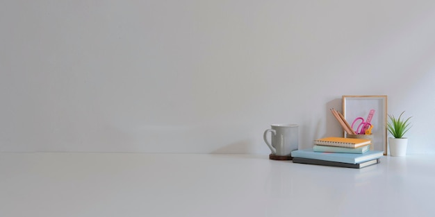 Posto di lavoro minimo con libri cornice tazza di caffè e pianta in vaso su tavolo bianco con copia spazio