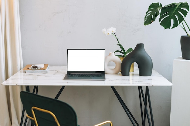 Posto di lavoro moderno con un laptop aperto con schermo bianco e monstera verde sul tavolo mock up modello