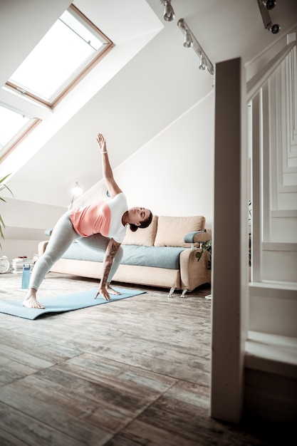 Postura yoga. Donna lavoratrice che piega la sua vita durante la sessione sportiva mentre si leva in piedi sul tappeto blu