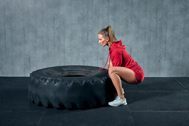 Potente, attraente ragazza muscolare impegnata in palestra, allenamento con pneumatici giganti in palestra.