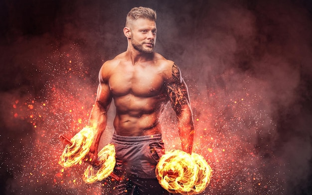 Potente bodybuilder elegante con tatuaggio sul braccio, facendo gli esercizi con i manubri. Concetto di arte del fuoco.