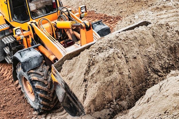 Potente pala gommata o bulldozer che lavora in una cava o in un cantiere Caricatore con un secchio pieno di sabbia Potente attrezzatura moderna per lavori di sterro