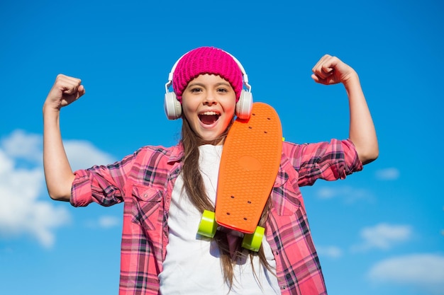 Potere della ragazza. Braccia della flessione del pattinatore felice sul cielo blu. Bambino con penny board all'aperto. Trucco della diapositiva di potenza. Parco giochi a frizione. Skatepark energetico. Il potere dello skateboard. Divertenti attività di fisica.