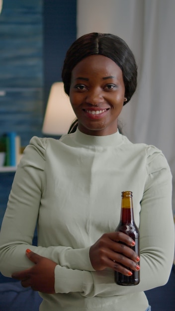 Potrait di donna afroamericana che sorride alla telecamera mentre tiene in mano una bottiglia di birra a tarda notte...