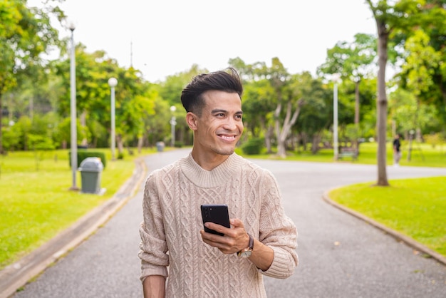 Potret pria muda tampan di taman selama musim panas menggunakan telepon