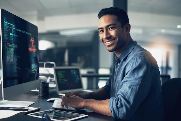 Potret seorang pria dan senyuman seorang programmer pada komputer di tempat kerja kantor pada malam hari, wajah TI dan pembuat kode pria atau orang yang melakukan pemrograman kode dan menulis untuk pengembangan perangkat lunak atau teknologi informasi