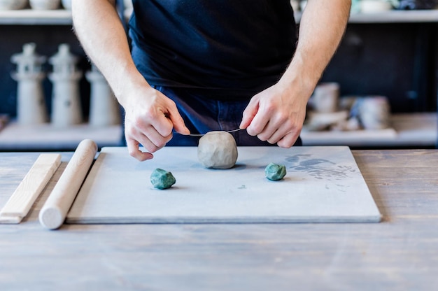 Potter argilla laboratorio ceramica arte concetto maschio tagli argilla cruda con il tagliacorda closeup sulle mani di uomo in piedi ceramista lavorare su un tavolo di legno con set di strumenti di scultura