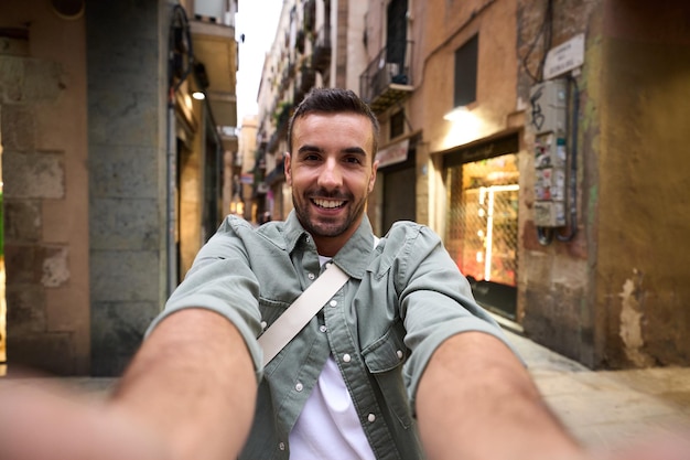 Pov giovane uomo bello sorride prendendo un selfie felice sulla strada turistica della città di Barcellona sullo sfondo